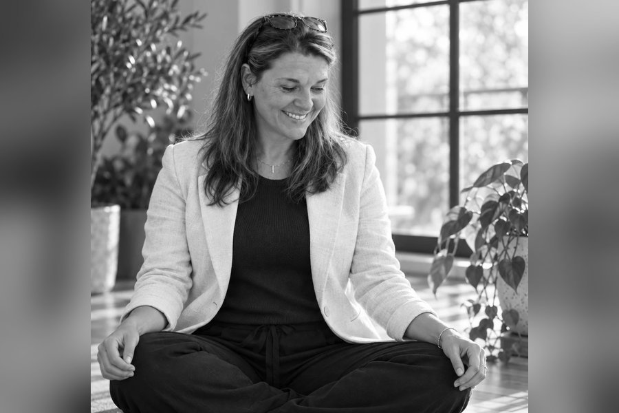Tara Nixon sitting cross-legged on a plum yoga mat in a sunlit room