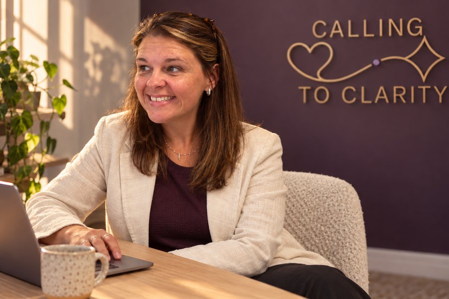Tara Nixon at her laptop in front of a Calling to Clarity sign
