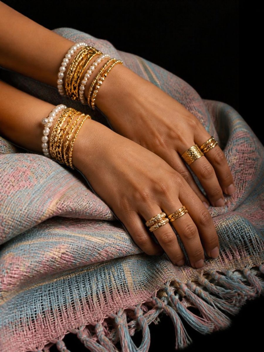 Hands with stacked gold rings and pearl bracelets on pastel woven cloth