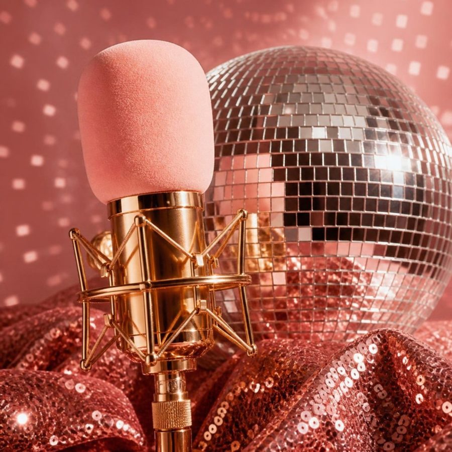 A gold microphone with a pink windscreen in front of a disco ball scattering light on a pink wall